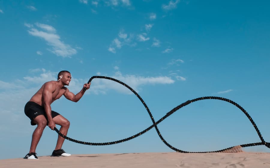 Man Standing on Brown Sand While Working out With Black Rope